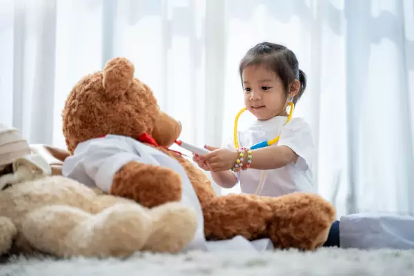 Baby playing as a doctor using a teddy as a patient. 